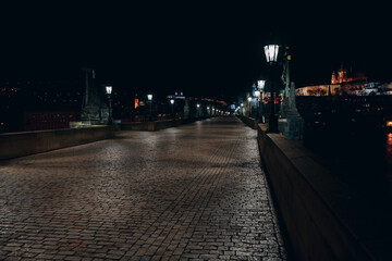 Fototapeta premium Street lights on the old stone Charles Bridge in the center of the city of Prague On the Vltava river at night and light from the street lights