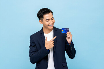Happy southeast Asian man in semi formal blazer pointing to credit card in light blue isolated...