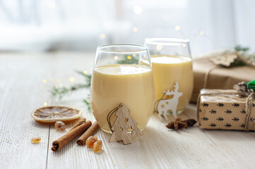 Two glasses of eggnog on a white wooden table next to the Christmas presents. Sweet egg dessert. Christmas breakfast.