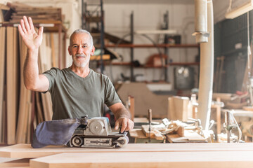 Smiling worker waving with a hand sander machine