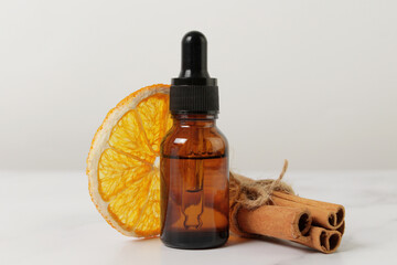 Winter essential aroma oil concept. Front view of various spices: cinnamon stick, dried orange slices around small brown medical oil bottle. Christmas