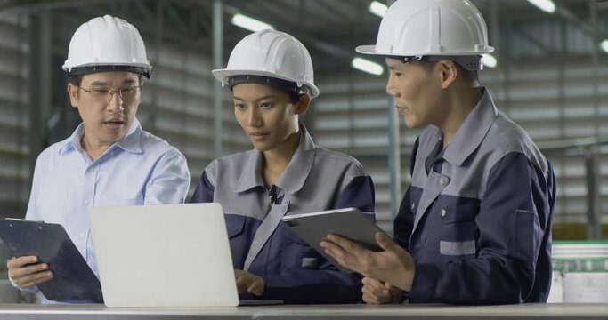Group of engineer working at factory. They looking to laptop to work together. They Work at the Heavy Industry Manufacturing Facility.