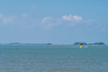 Naklejka premium Small fishing boat motoring behind yellow lighthouse