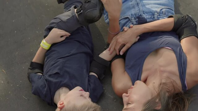 From-above shot of loving mother and her 7-year-old son in knee and elbow pads and sportswear lying on skateboarding rink holding hands