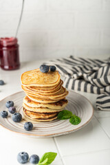 sweet pancakes for breakfast in a stack. on a ceramic plate. with fresh blueberries and mint. light key vertical position