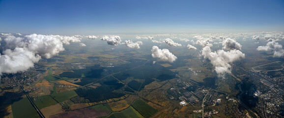 Aerial view from airplane window at high altitude of distant city covered with white puffy cumulus...
