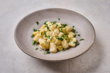 Close up traditional Alpine dish gnocchi, prepared with potato and whole grain flour dough with cream sauce and parsley on gray ceramic plate