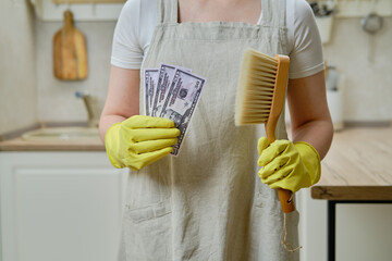 A woman holds money in dollars while cleaning a home kitchen, close-up