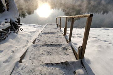 Snowy staircase to the lake in the forest on sunset
