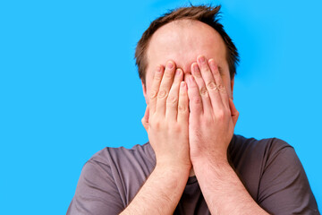 Portrait of a crying adult man with a disheveled appearance, blue studio background