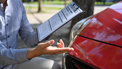Insurance officer examining car and filing report claim form after accident.