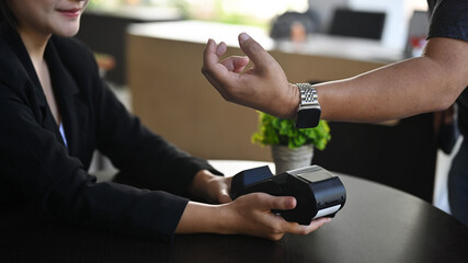Cropped shot man customer using terminal for contactless payment with smartwatch in coffee shop.
