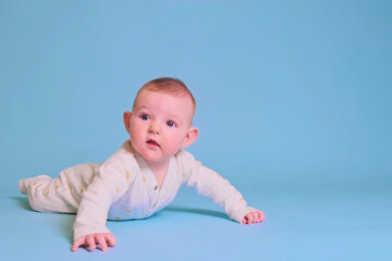 Infant baby boy looks with curiosity while lying on his tummy, studio blue background. Four month old child, copy space