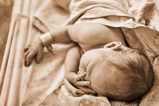 A newborn baby with a maternity hospital bracelet on his arm is sleeping in a crib. A newly born child in a clinic bed behind a transparent glass