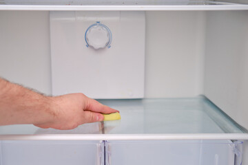 A man hand with a yellow sponge washes the refrigerator