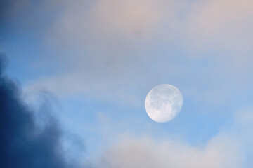 The moon in the day blue sky amid smoke and dark clouds