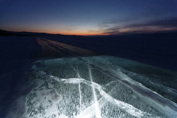 The sunset and frozen lake, ice with with cracks. Lake Baikal