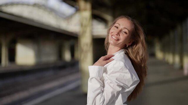 Portrait of a happy blonde woman on a sunny day on the platform of the old train station in a white shirt walking and enjoying life
