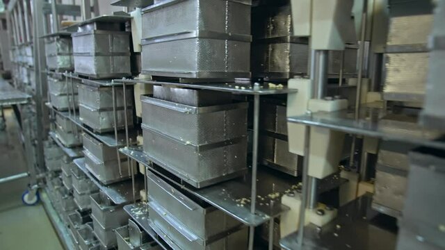 Numerous stainless steel containers for butter. Steel reticulated boxes for butter stored on the tall metal shelves. Modern dairy enterprise.