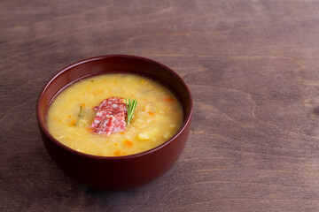 vegetable soup with meat.Split pea soup with ham, carrots and potatoes on a rustic wooden background.Classic Dutch pea soup erwtensoep, snert with bacon in the brown bowl on the table with copy space.