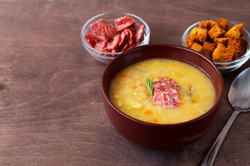 soup with meat. Split pea soup with ham, carrots and potatoes on a rustic wooden background. Classic Dutch pea soup erwtensoep, snert with bacon in the brown bowl on the table with copy space.
