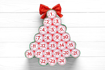 Advent calendar in shape of Christmas tree with numbers and ribbon instead of star on white wooden table Xmas advent calendar concept Top view Flat lay Holiday card