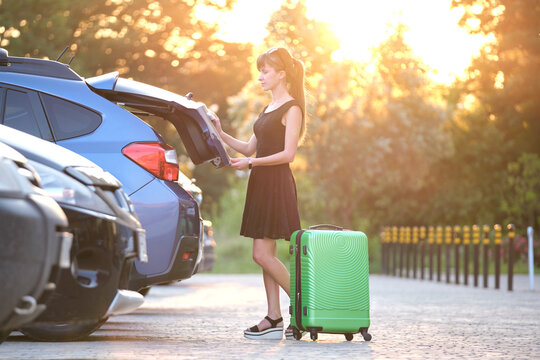 Young Female Driver Taking Out Luggage Suitcase Bag Out Of Her Car. Travelling And Vacations Concept