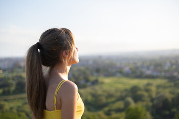 Young relaxed woman standing in green field looking at sunset view in evening nature. Relaxation and meditation concept