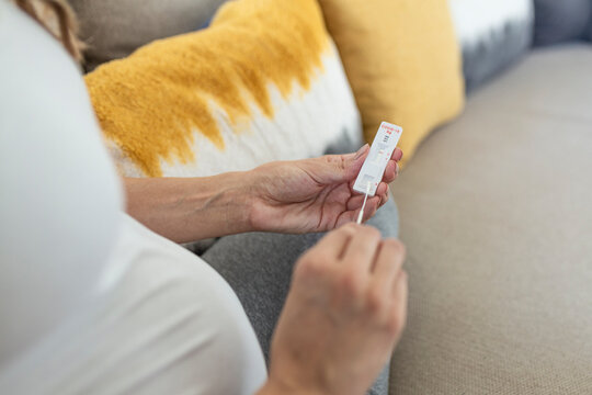 Pregnant woman sitting at a living room of a house with people, introducing a nasal swab in the nose