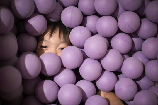 little child looking happy covered by purple balls in ball pit or pool