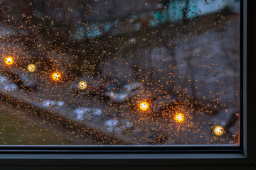 Raindrops on a window pane against the background of a blurred cityscape on a cloudy morning.