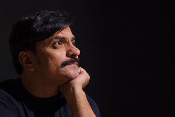 Side view of a common man with his hand on chin with black background