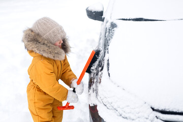 Girl is brushing snow from a car. Clearing the ice of snow after a blizzard and heavy snowfall....