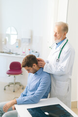 Fototapeta premium Vertical shot of mature adult male manual therapist turning and bending head of male patient to check his injured neck. Young man on preventive examination of doctor chiropractor on neck diagnostic.