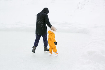 A father teaches a child to skate on the cleared ice of a frozen lake in the countryside. Dad leads his daughter by the hand, insuring her from falling. 
 Ice skating season on winter frosty days