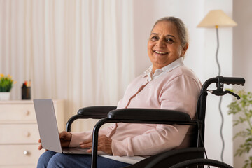 Senior woman on wheel chair looking at camera with smile while using laptop
