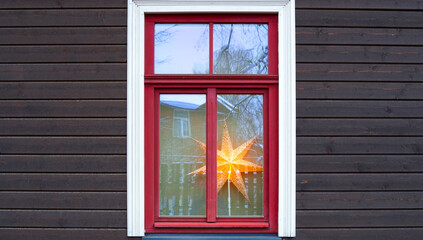 Wall of a wooden private house with a red window frame. Christmas star on the windowsill. Winter.