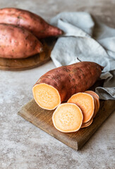 Whole and slices raw sweet potatoes on wooden kitchen board, organic yam. The farm food.