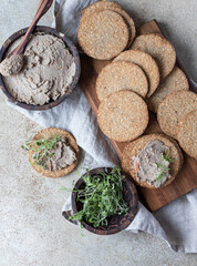 Homemade meat or chicken liver pate with multigrain crackers and microgreen, concrete background. Top view.