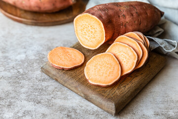 Whole and slices raw sweet potatoes on wooden kitchen board, organic yam. The farm food.
