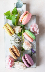 Various types of colorful macarons or macaroons decorated with flowers on light background. Traditional french almond dessert with sweet filling.