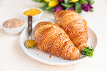 Breakfast with fresh croissants, chocolate cream, jam and colorful tulips on light stone background. Beautiful romantic composition.
