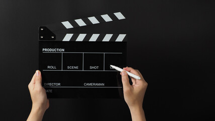 Hand is holding black clapper board or movie slate and marker Pen on black background