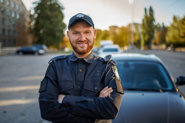 Male police officer in uniform poses near the car