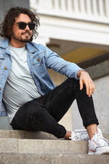 a stylish guy with glasses stone wall on the background and looks away. strong and strict male. in casual clothes