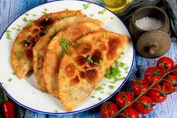 Hot homemade chebureki pies with minced meat, onion and pepper on plate, wooden background