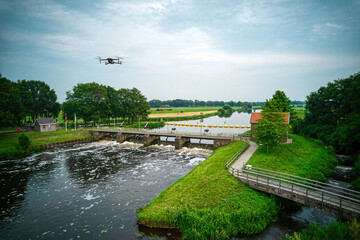 An aerial view with drone in the background above a weir in the river Vecht in the Netherlands. Downstream, Sluiswachtershuis next to the bridge. Fish pass, fish ladder. Overijssel Vecht