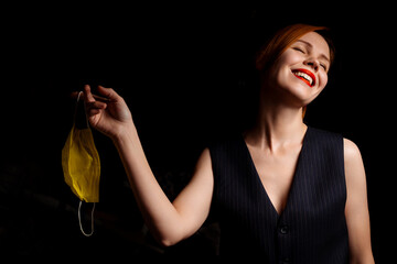 Freedom from the medical mask. Woman laughs contentedly holding a medical mask in her hand on a dark background.