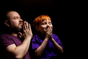 Dad and son are praying on a black background.