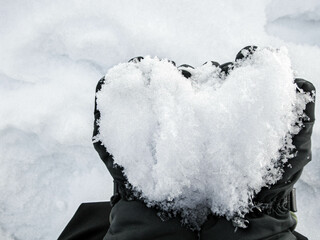 Close Up Of Hands holding a snowball shaped like a heart against the a background of white snow. Romantic gesture and symbol